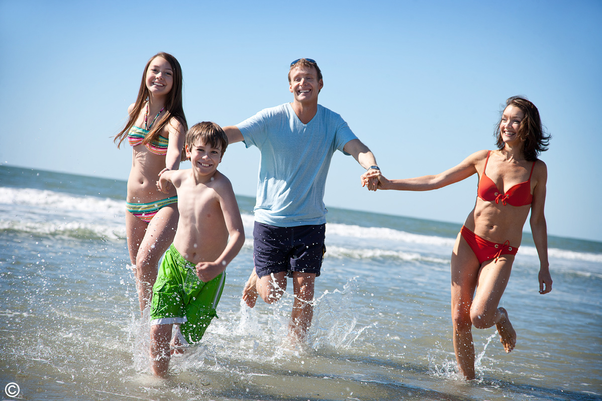 family running along the beach shoreline on a sunny day