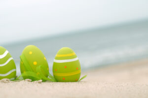 Easter decorated eggs on sand. Beach and ocean in the background.